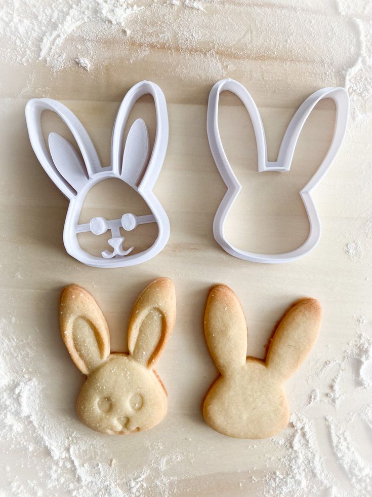 Bunny-shaped cookie cutters and matching cookies on floured surface, perfect for Easter baking fun.
