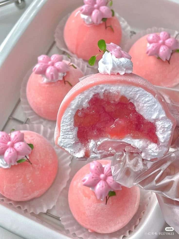 Pink mochi dessert with floral decoration and creamy filling on display. Elegant, sweet treat in soft pastel hues.