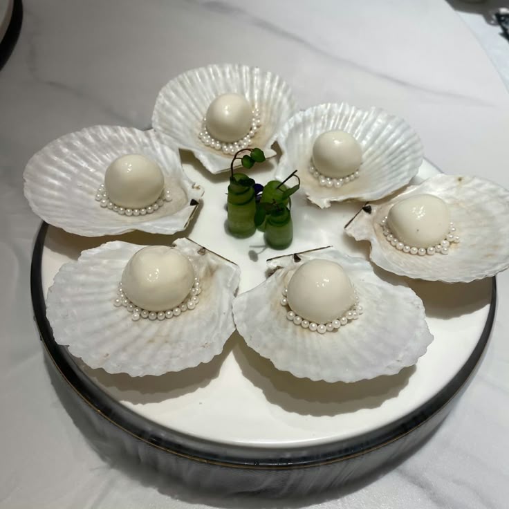 Elegant dessert with white chocolate pearls in scallop shells on a white plate, garnished with green leaves.