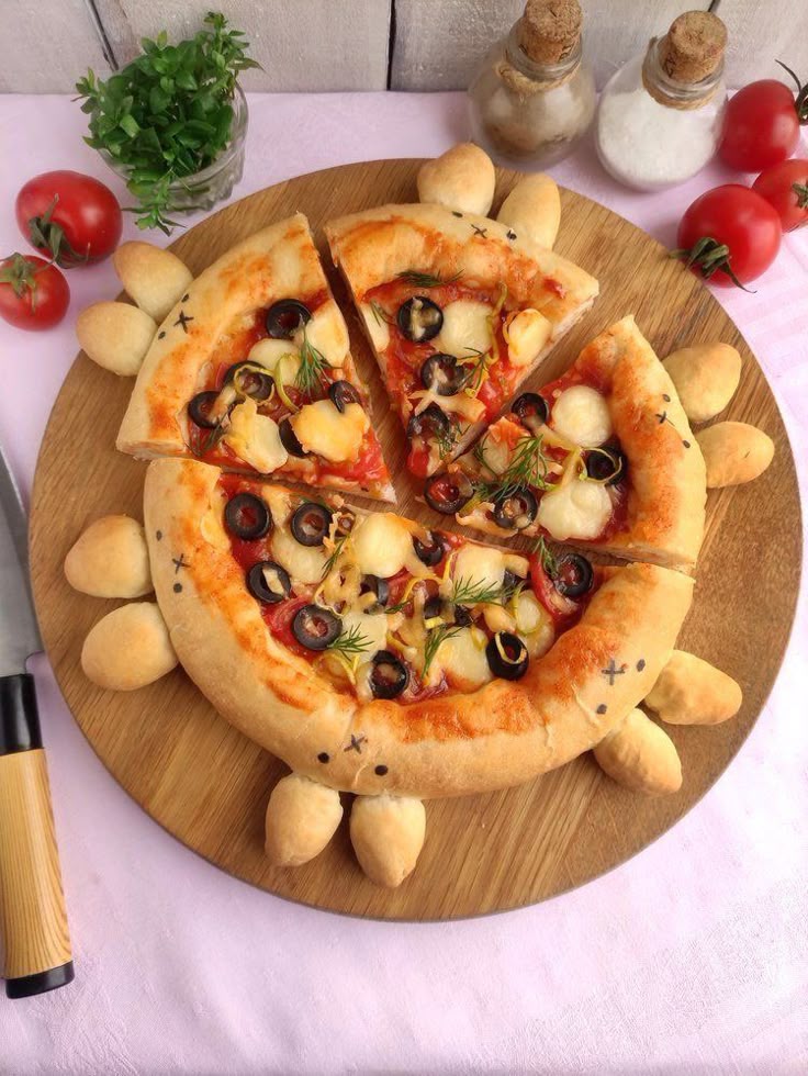 Creative pizza design with olives, cheese, and herbs on a wooden board, surrounded by fresh tomatoes and spices.