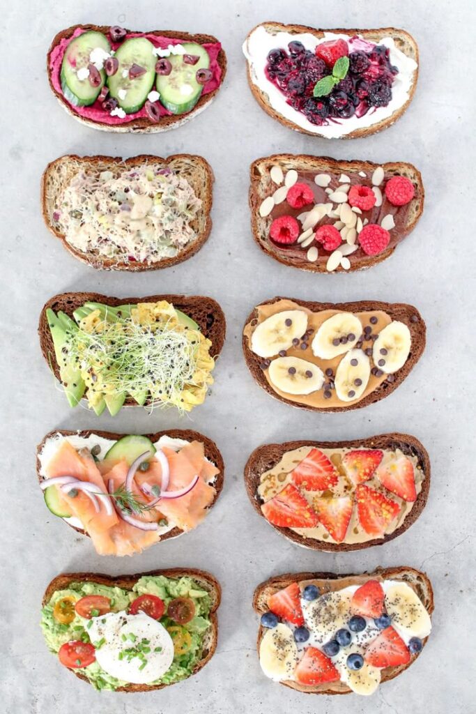 Variety of gourmet toasts with fresh toppings like fruit, avocado, and berries on a concrete background.