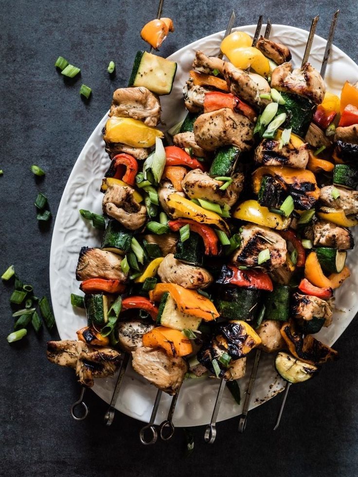 Grilled chicken and vegetable skewers on a white plate, garnished with chopped green onions, ready to serve.