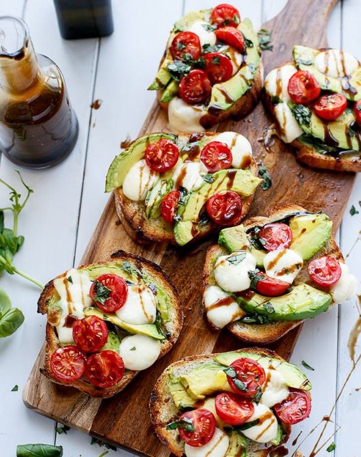 Avocado toast topped with fresh mozzarella and cherry tomatoes on a wooden board with balsamic drizzle.