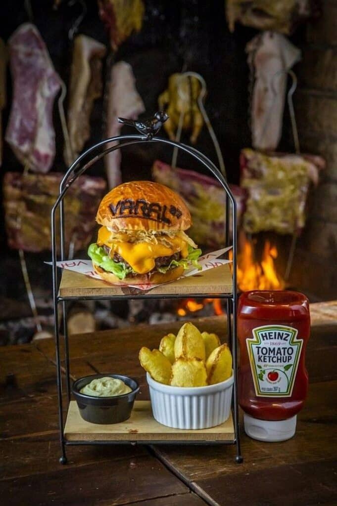 Juicy burger with cheddar, fries, and dipping sauce, grilled meat background, Heinz ketchup bottle beside, cozy setting.