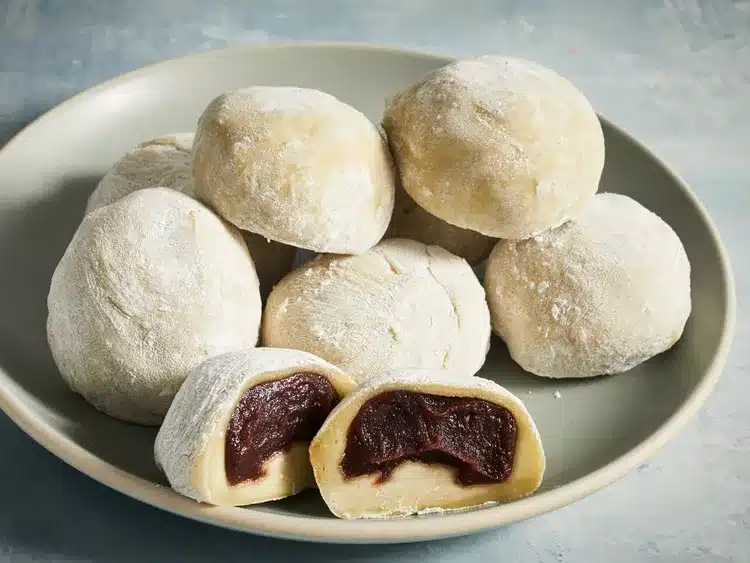 Plate of homemade daifuku mochi with sweet red bean filling, dusted with rice flour for a soft, chewy texture.