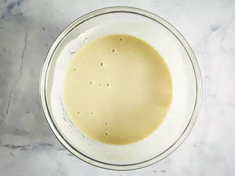 Smooth pancake batter in a clear glass bowl on a marble countertop, ready for cooking breakfast pancakes.