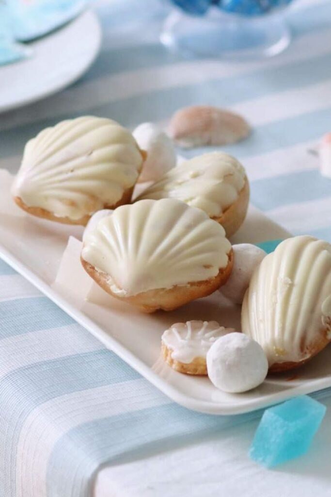 Seashell-shaped cookies with white icing on a tray, perfect for a beach-themed party or coastal dessert table.