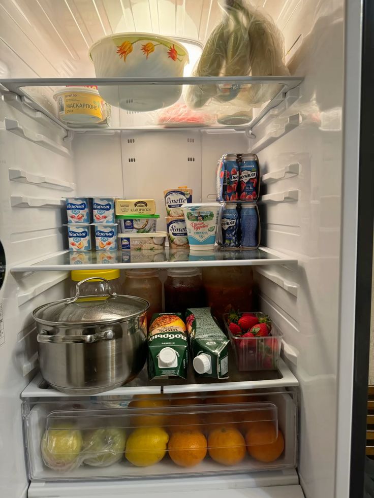 Open fridge with assorted groceries: dairy products, beverages, fruits, vegetables, and a stock pot.