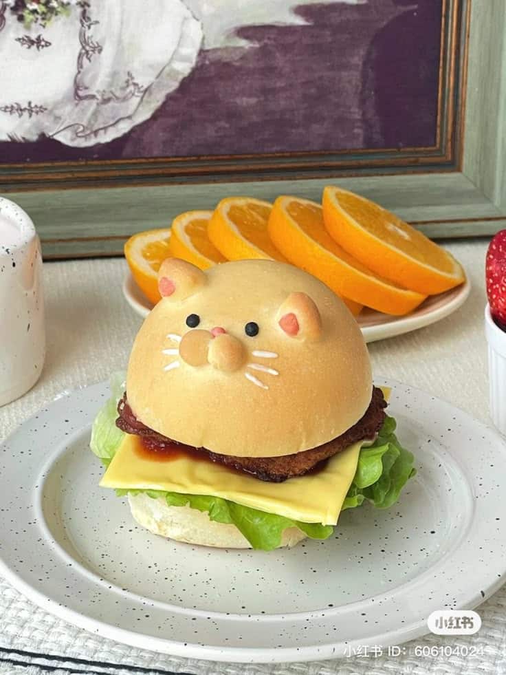 Cute cat-shaped burger with lettuce, cheese, and slices of oranges on the side, perfect for a fun meal presentation.