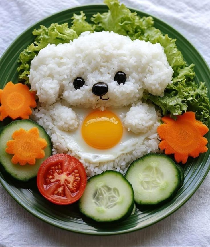 Cute rice and egg dish shaped like a puppy, surrounded by fresh vegetables on a green plate.