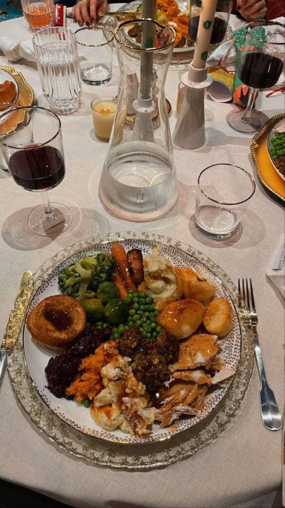 Festive dinner with roasted vegetables, turkey, stuffing, Yorkshire pudding, wine, and water on an elegant table.