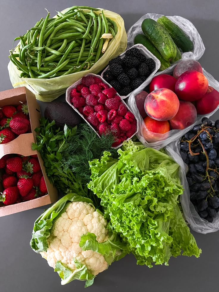 Fresh fruits and vegetables assortment, including berries, lettuce, green beans, and cauliflower on a gray background.