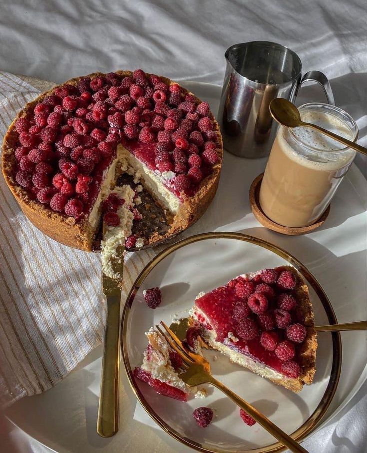 Raspberry cheesecake with two golden forks, coffee, and milk jug on a table, perfect for a delicious breakfast.