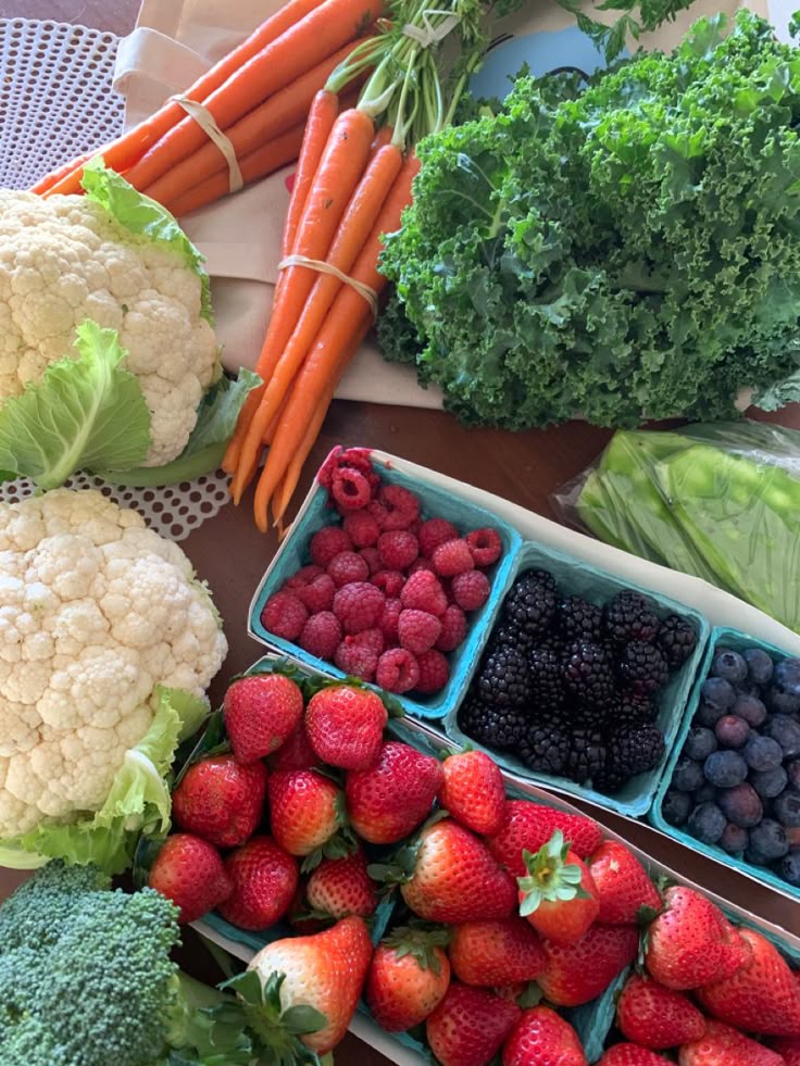 Assorted fresh fruits and vegetables, including strawberries, raspberries, carrots, kale, and cauliflower on a table.