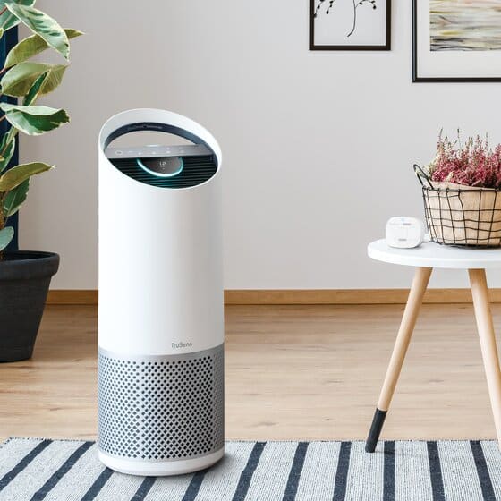 Sleek white air purifier in modern living room setting, placed beside a table with plants and decor.
