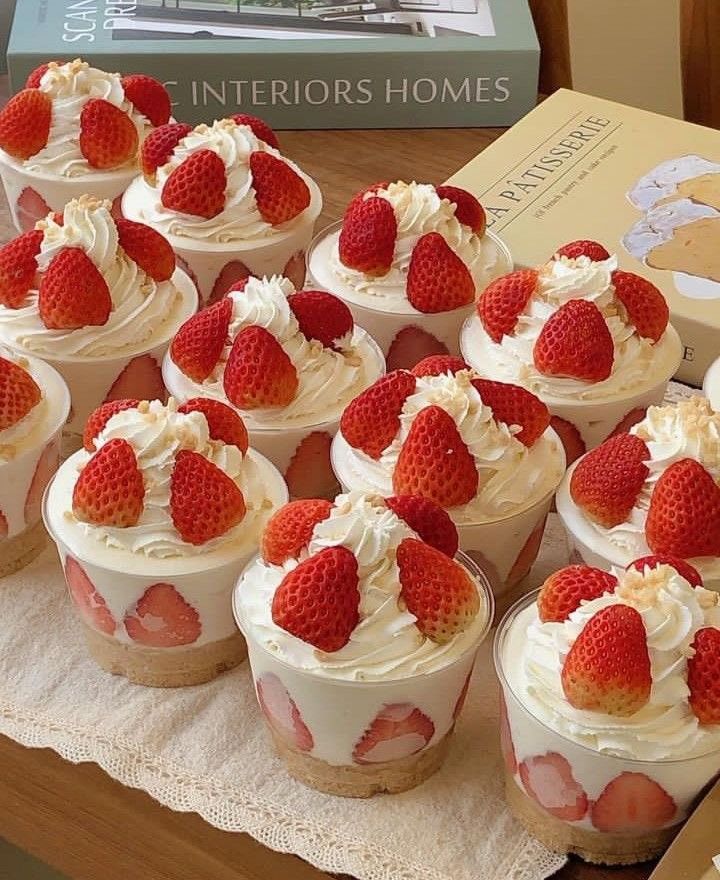 Strawberry cream parfaits topped with fresh strawberries and whipped cream on a wooden table.