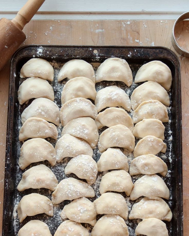 Homemade pierogi with flour, ready to cook on a baking tray, accompanied by a rolling pin and a cutter.
