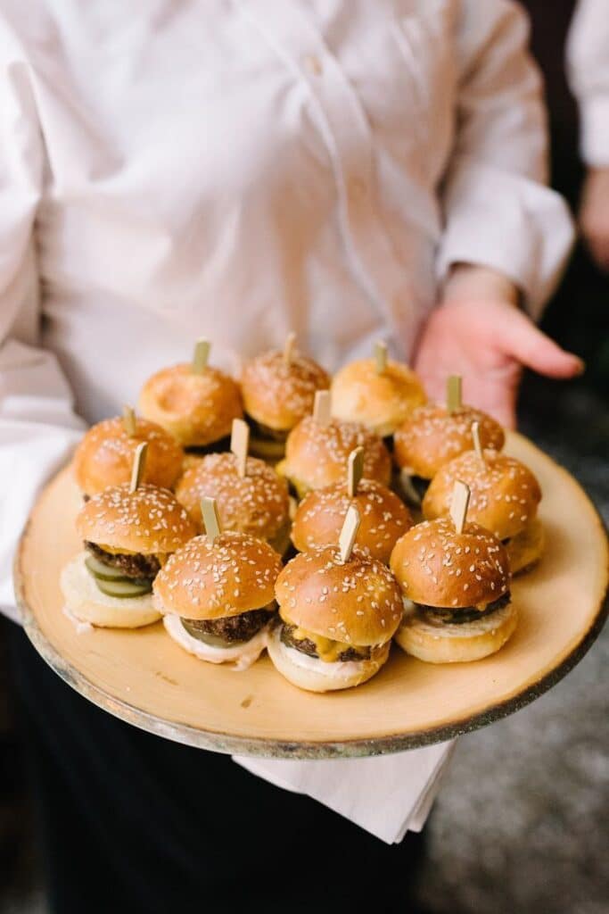 Plate of mini cheeseburgers with sesame buns served at an event for appetizers or party snacks.