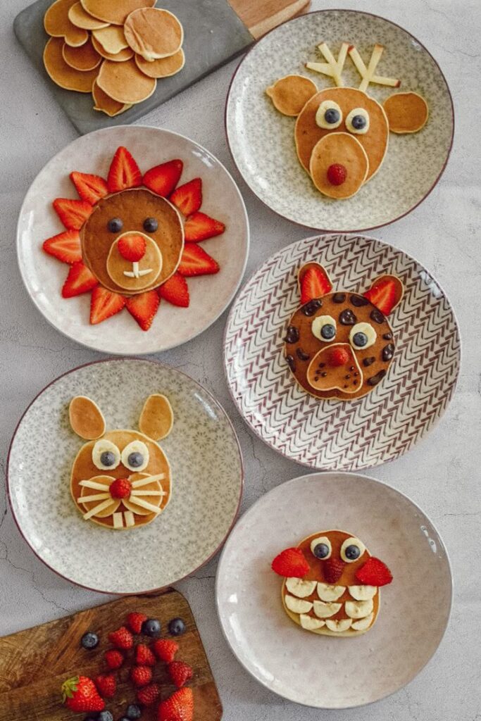 Animal-themed pancakes on plates with creative fruit decorations, featuring bunny, lion, and owl designs.