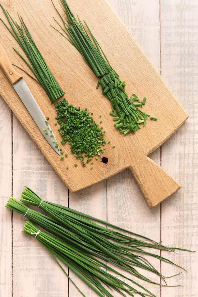 Fresh chives on a cutting board with a knife, showing whole and chopped herbs for cooking and garnish.