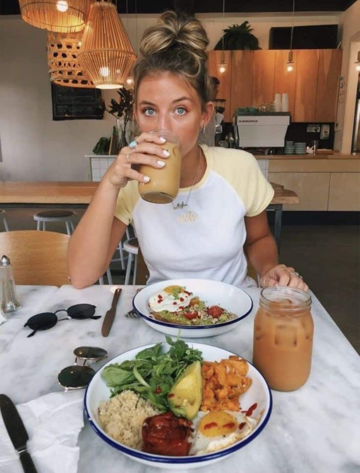 Woman enjoying iced coffee and healthy brunch at modern café.