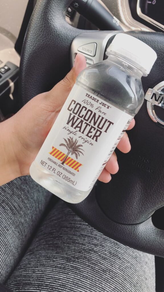 Hand holding Trader Joe's coconut water bottle in a car. Refreshing drink on a drive.