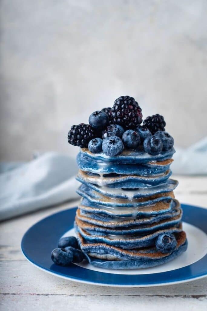 Stack of blue pancakes topped with fresh blueberries and blackberries on a blue plate.