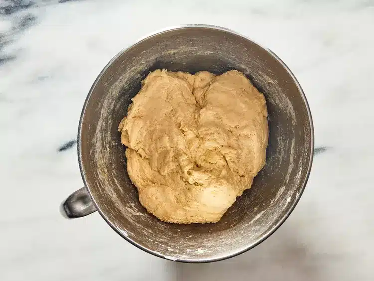 Smooth bread dough in a metal mixing bowl on a marble surface, ready for baking.