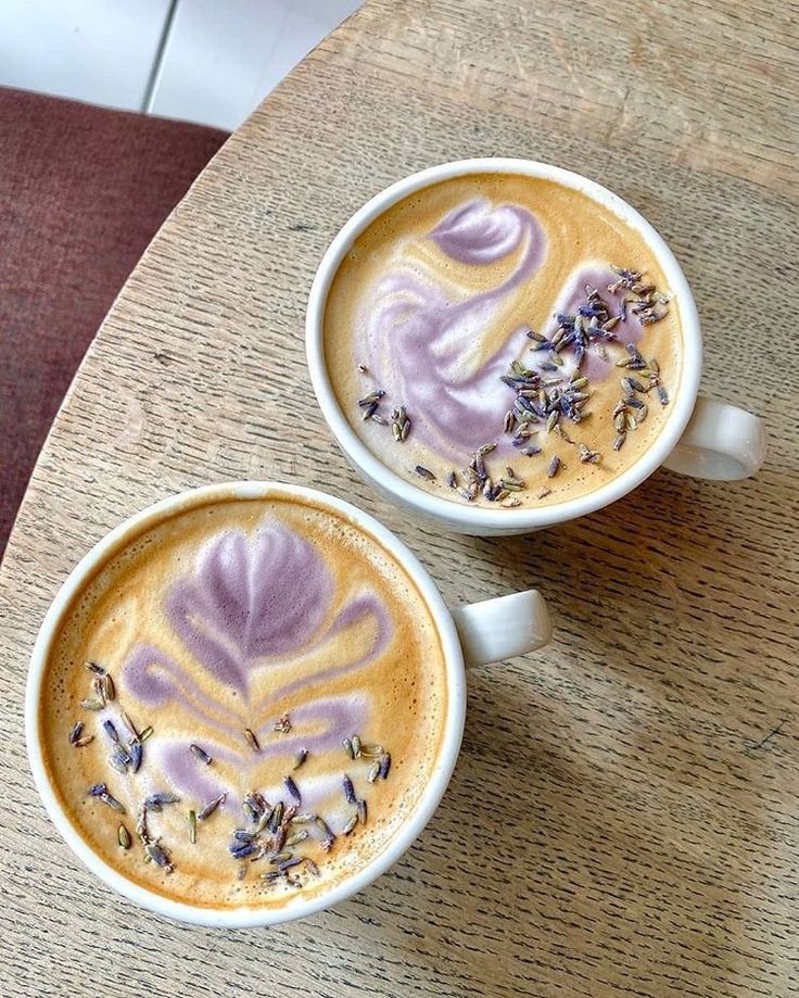 Lavender lattes with purple latte art on a wooden table, topped with dried lavender sprigs. Cozy coffee atmosphere.