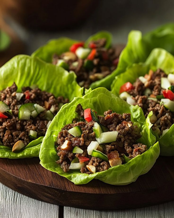 Lettuce wraps with ground beef, chopped vegetables, and nuts on a wooden platter, perfect for a healthy meal.