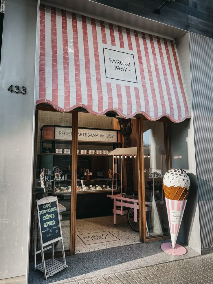 Vintage ice cream shop with pink striped awning, large cone decor, and sidewalk chalkboard menu featuring crepes and coffee.