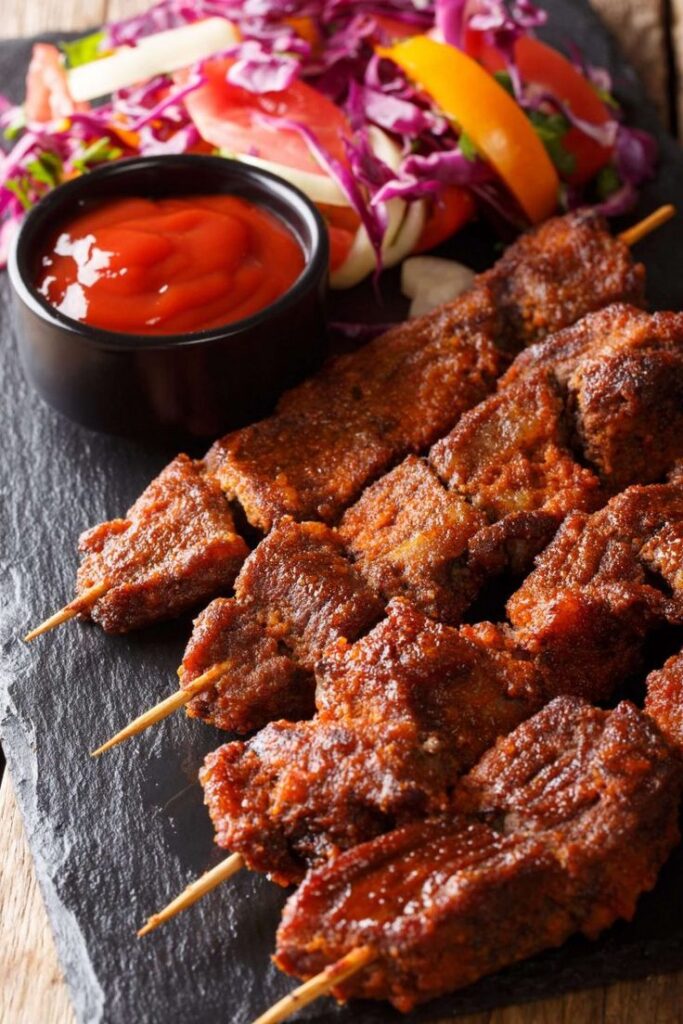 Grilled spicy beef skewers with fresh salad and dipping sauce on a slate platter.
