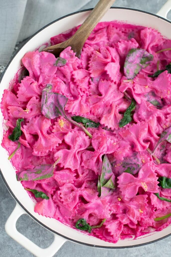 Vibrant pink pasta with greens in a white pot, perfect for a colorful and delicious meal.