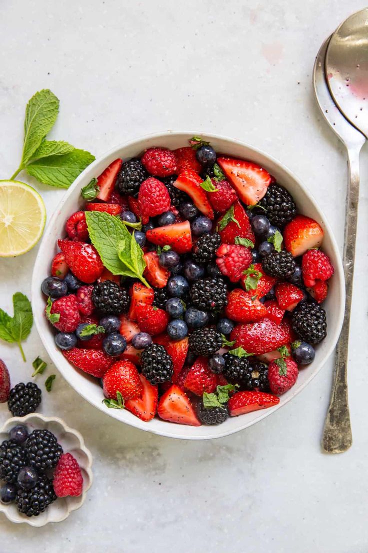 Bowl of fresh mixed berries with strawberries, blueberries, blackberries, raspberries, and mint on a white background.