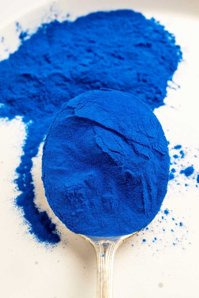 Blue spirulina powder on a silver spoon, perfect for smoothies and health recipes.