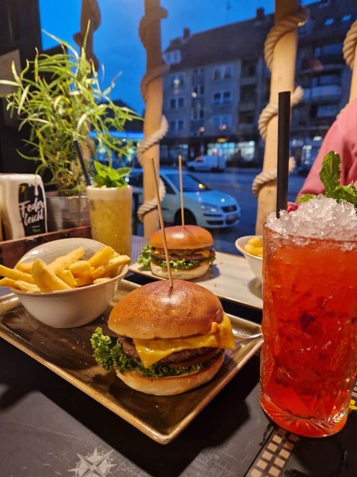 Cheeseburger and fries with iced drink on a table at a cozy restaurant near a window at dusk.