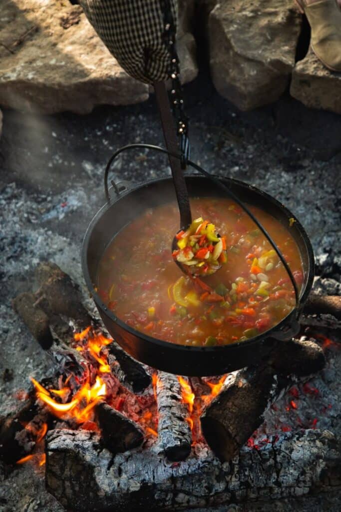 Hearty vegetable stew cooking over an open campfire in a black cauldron. Perfect for outdoor cooking enthusiasts.