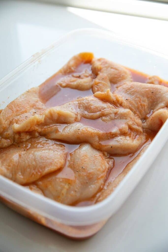 Marinated chicken breast in plastic container, ready for grilling or cooking.