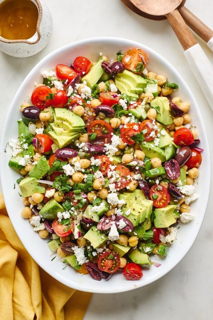 Fresh Mediterranean salad with avocado, cherry tomatoes, chickpeas, olives, and feta on a white plate with dressing.