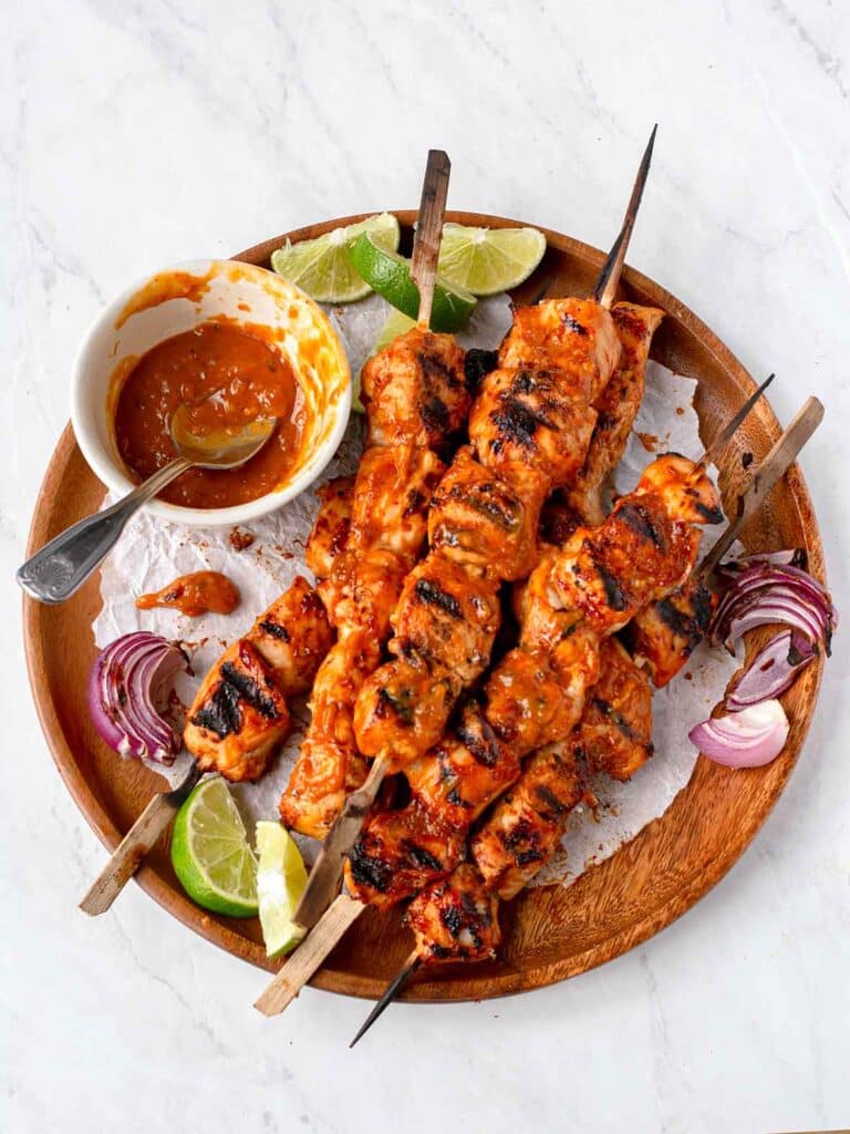 Grilled chicken skewers with spicy sauce, lime wedges, and red onions on a wooden platter. Perfect for BBQ gatherings.