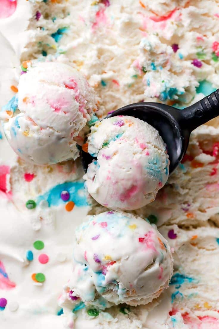 Colorful birthday cake ice cream scoops with sprinkles in black scoop on white ice cream background.