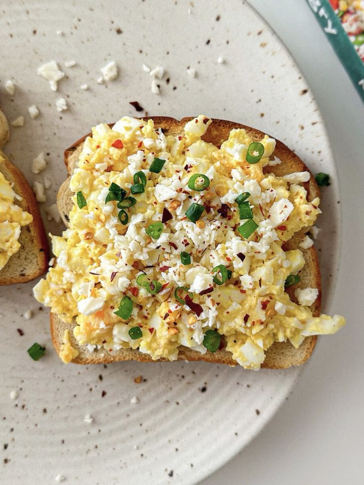 Scrambled egg toast topped with crumbled feta, green onions, and red pepper flakes on a beige plate.