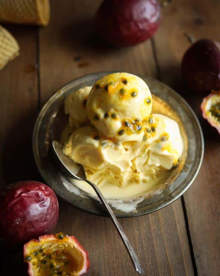 Delicious passion fruit ice cream in bowl with fresh passion fruits on rustic wooden table.