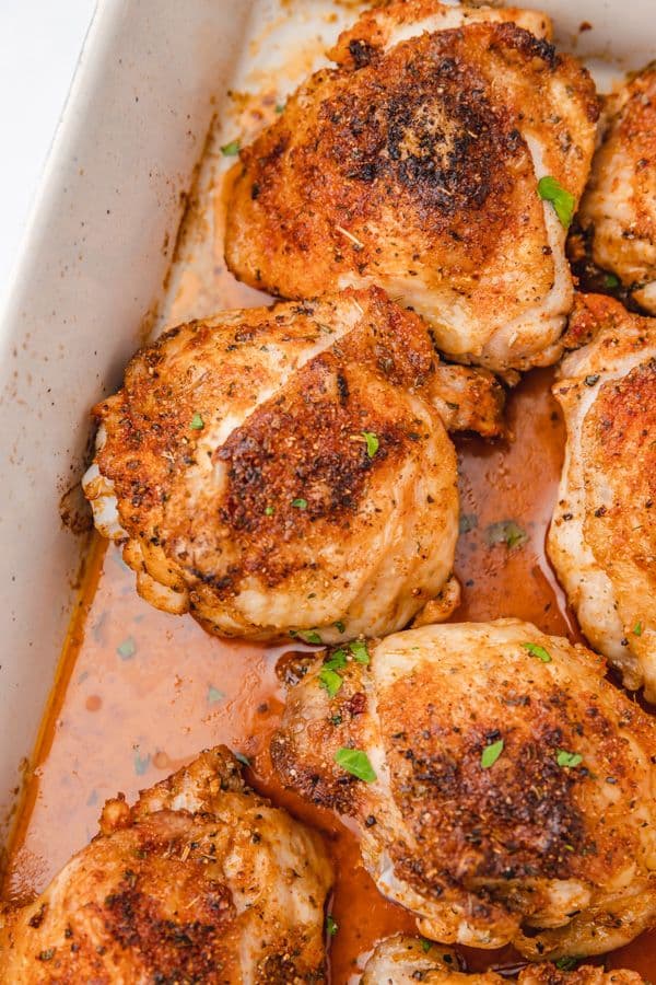 Juicy baked chicken thighs seasoned with herbs and spices, set in a roasting pan with a flavorful glaze.