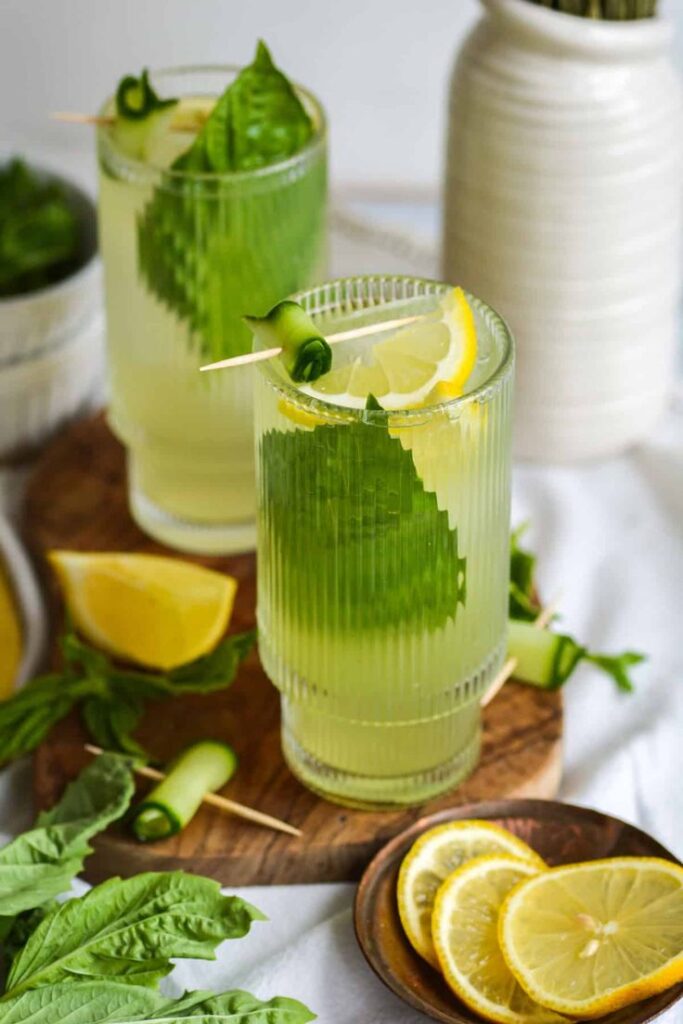 Refreshing summer cocktail with cucumber, lemon, and basil in a glass, garnished with lemon slices and cucumber.