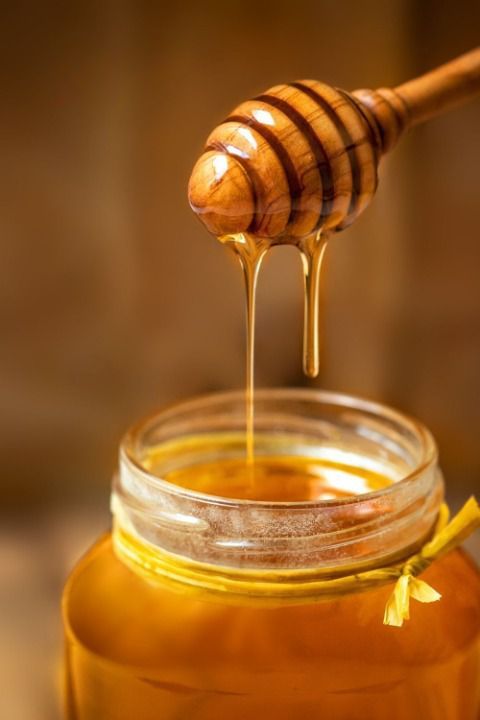 Drizzling honey from dipper into glass jar, rich golden color, close-up shot.