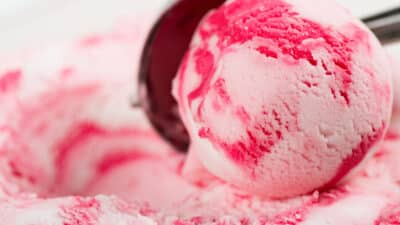 Close-up of a pink and white ice cream scoop with swirls, showcasing creamy texture and vibrant colors.