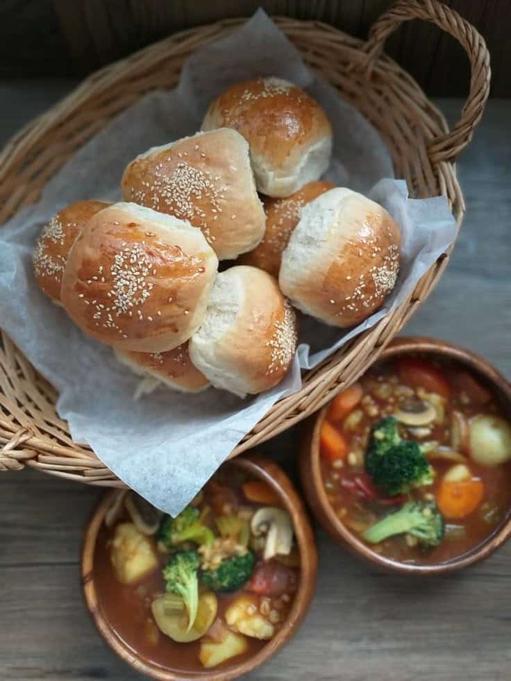 Basket of fresh sesame buns with two bowls of hearty vegetable stew on a wooden table.