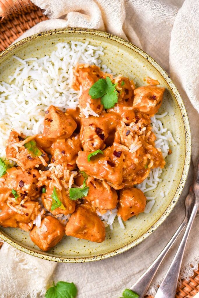 Creamy butter chicken curry with basmati rice, garnished with cilantro, served in a rustic bowl.