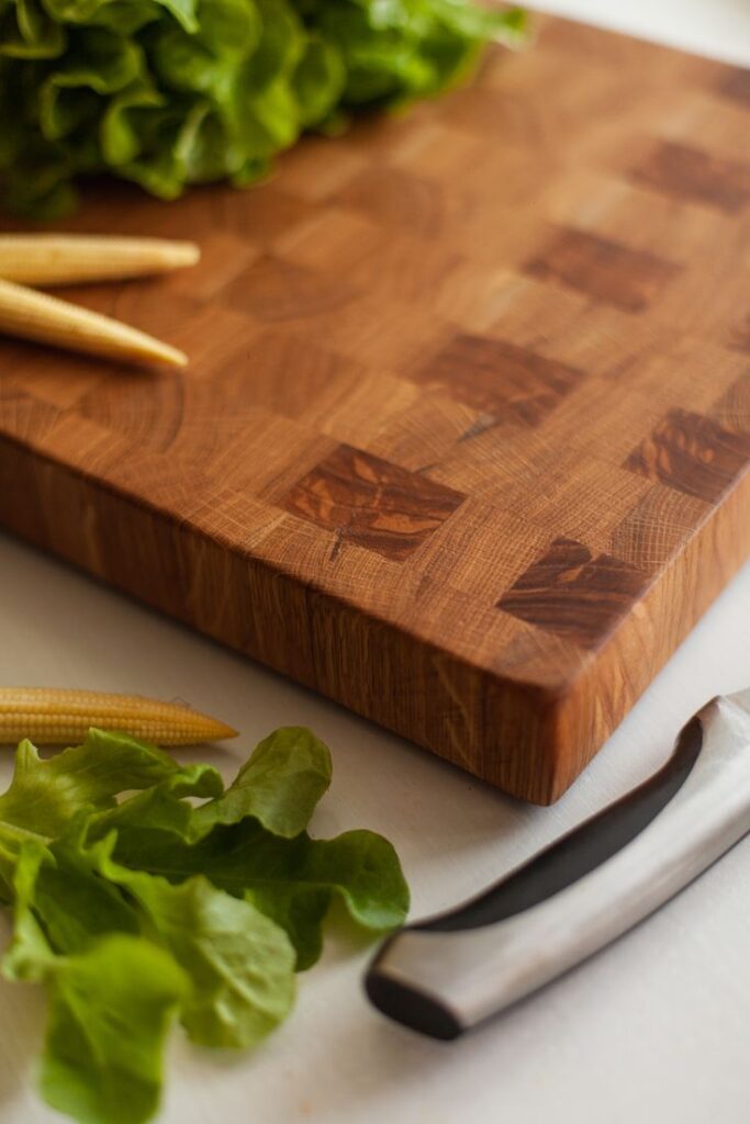 Wooden cutting board with fresh lettuce, baby corn, and a kitchen knife on a white surface. Ideal for cooking prep.